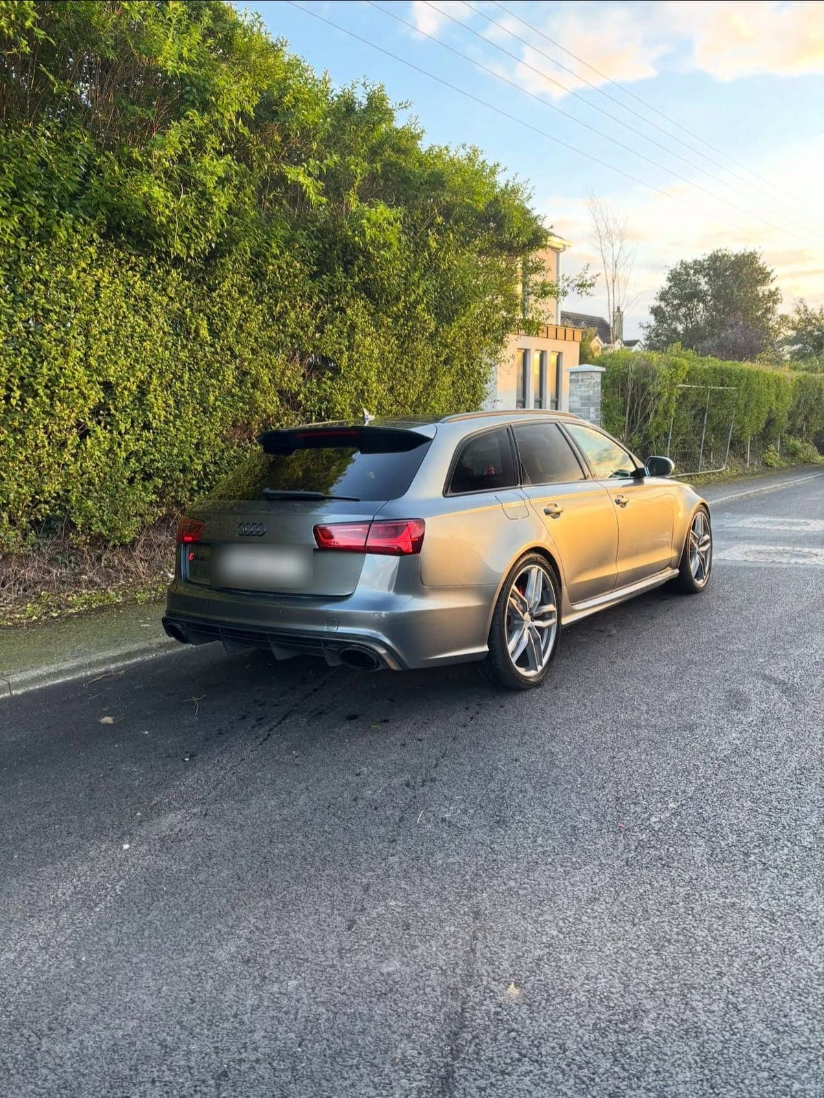 Grey Audi RS6 Avant from the rear three quarter, parked on a quiet road at sunset